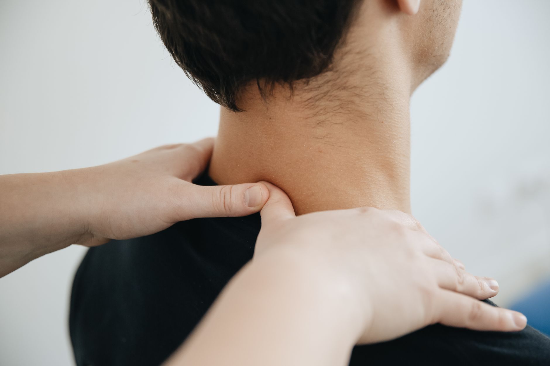 男性が子どもの首元を優しく支え、指を薄く皮膚に触れて、皮膚をほんの少しだけ牽引しているように触れているクローズアップ。